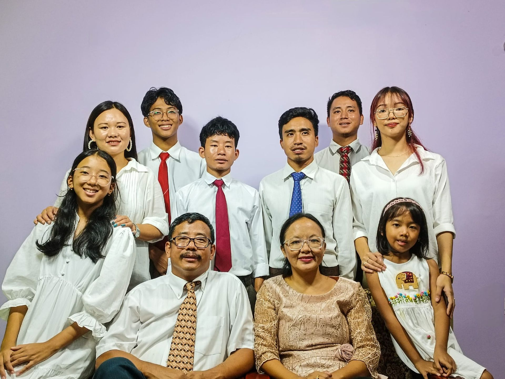 Nine people in white shirts pose for a group portrait against a purple background.