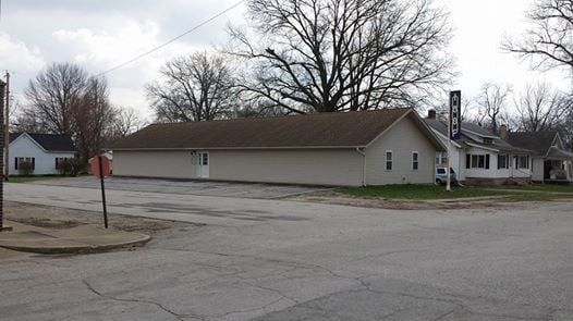 Quiet residential street with a beige building, leafless trees, and an overcast sky