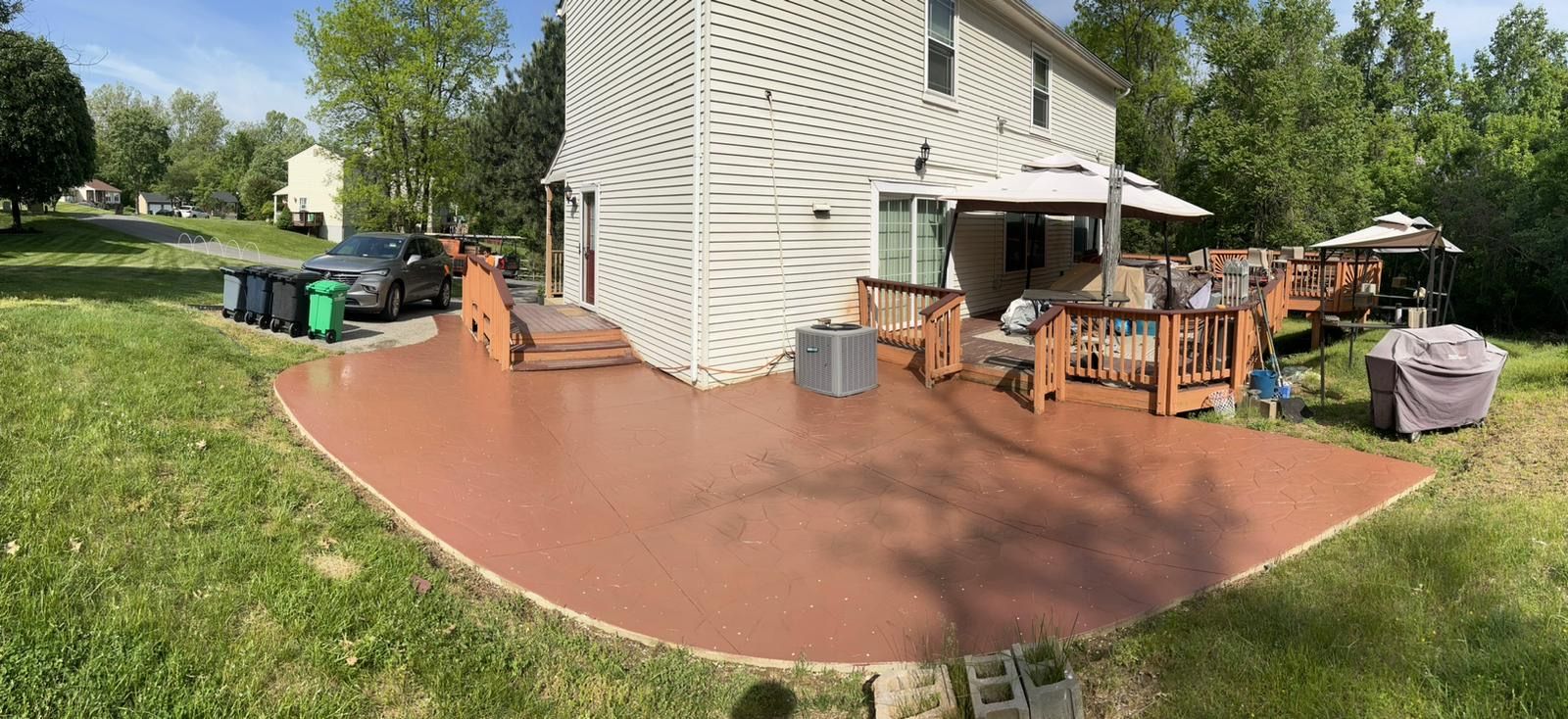 Backyard patio with outdoor furniture beside a house, green lawn, and trees on a sunny day