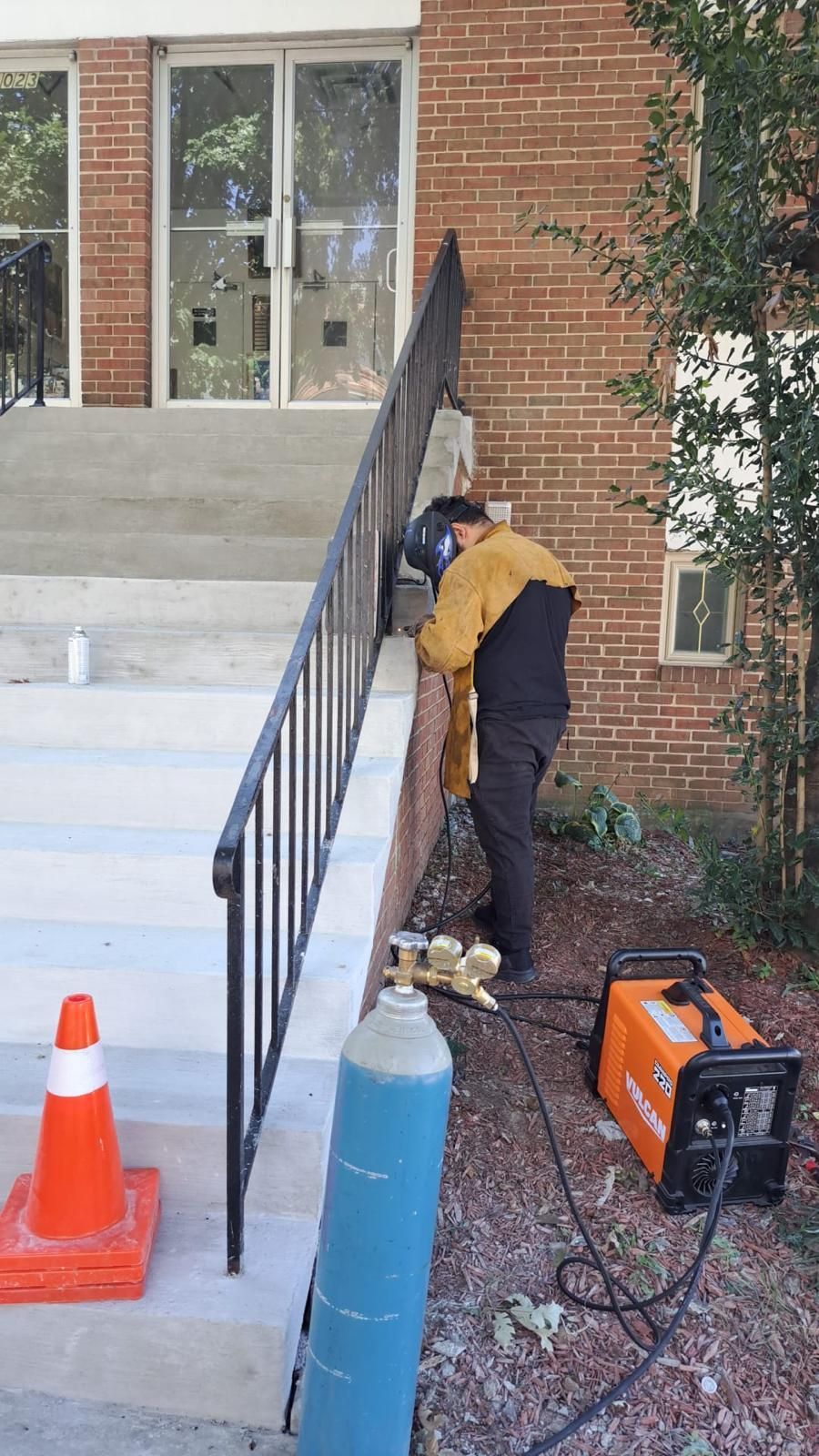 Worker using power equipment beside outdoor stairs and brick building entrance