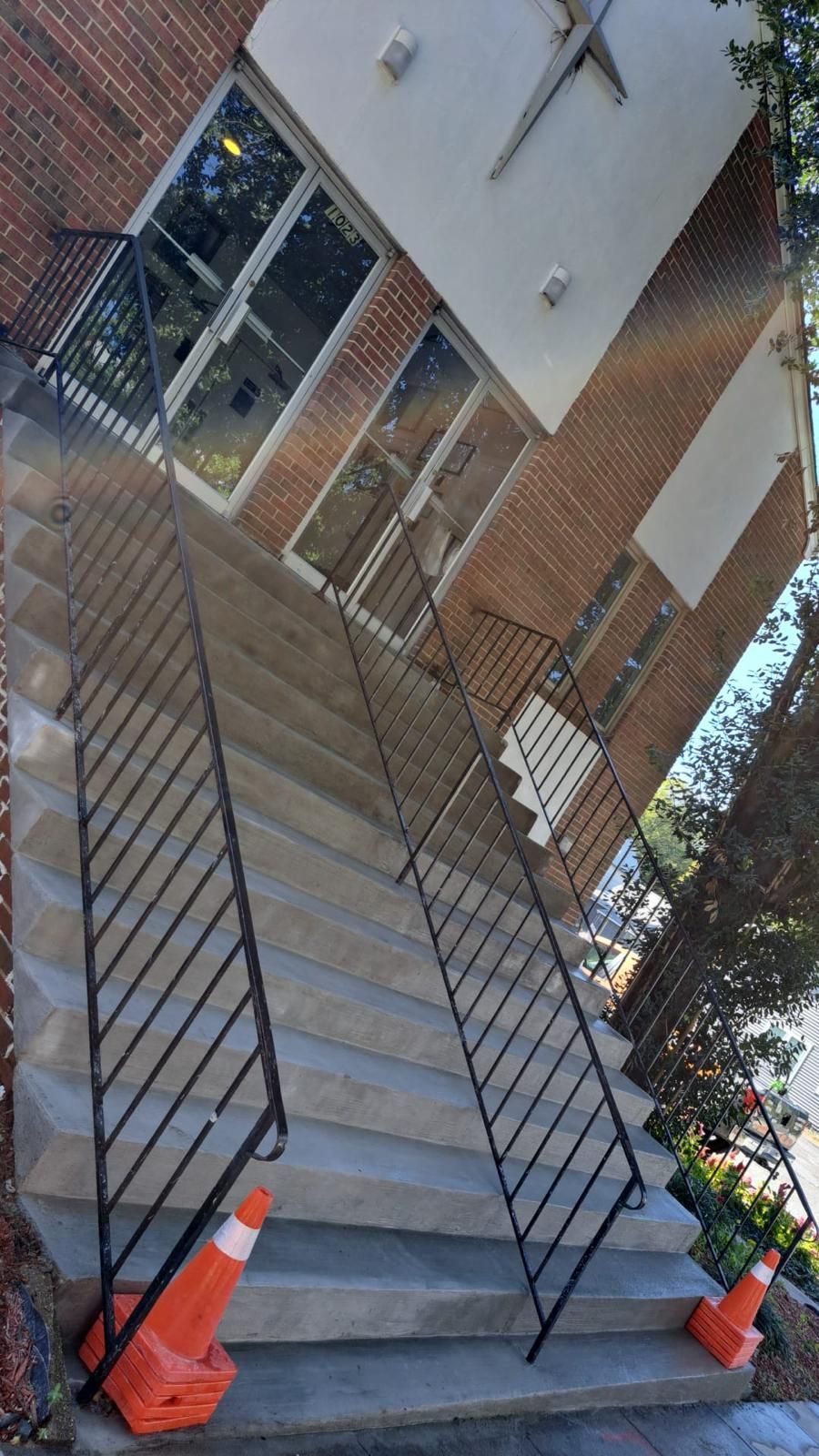 Stairway blocked by black railings and two orange cones beside a brick building entrance