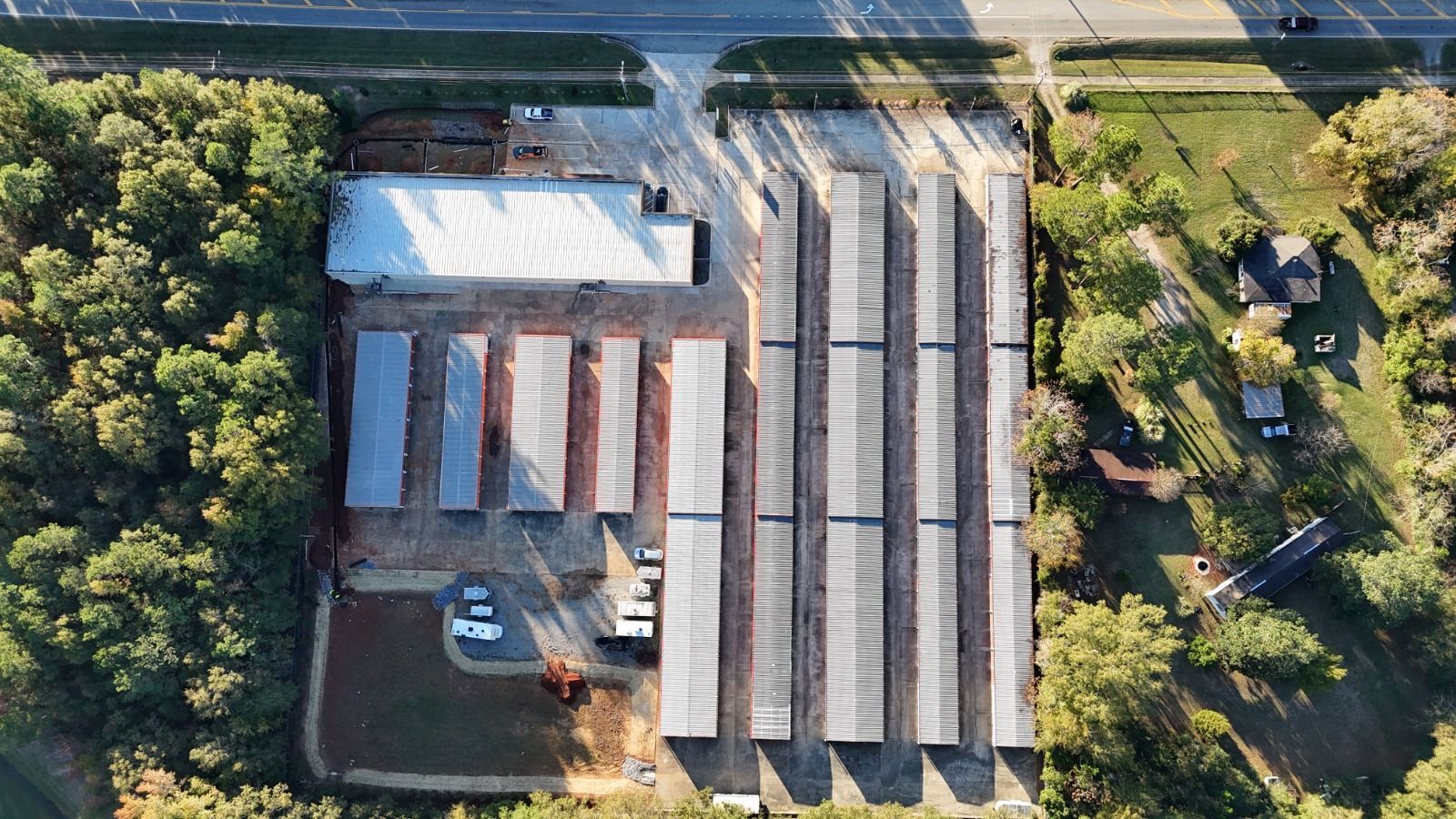 Aerial view of a farm with long white-roofed buildings, red storage sheds, and surrounding trees and fields