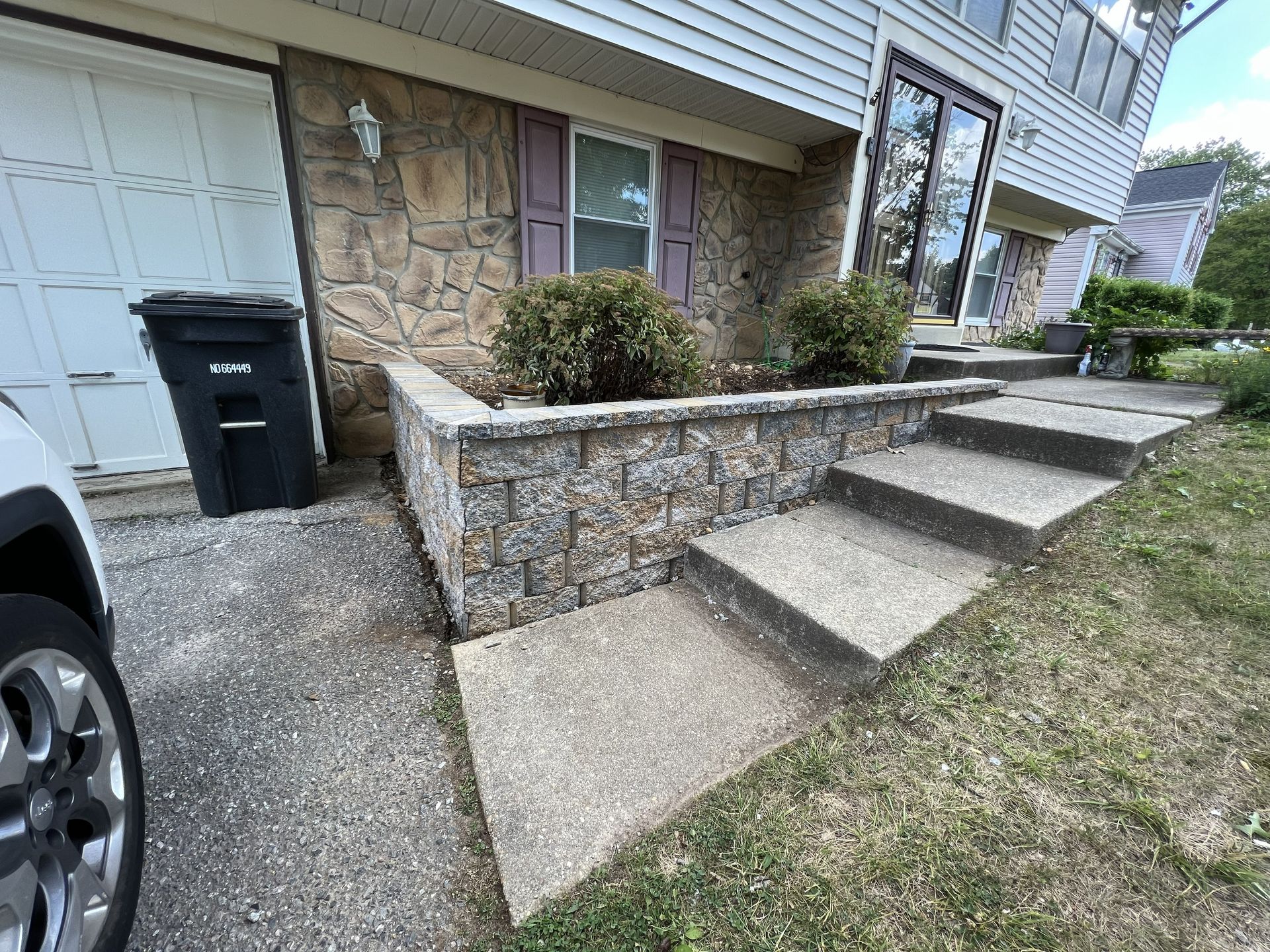 Front steps and stone retaining wall beside a house, with a wheelchair ramp and driveway visible.