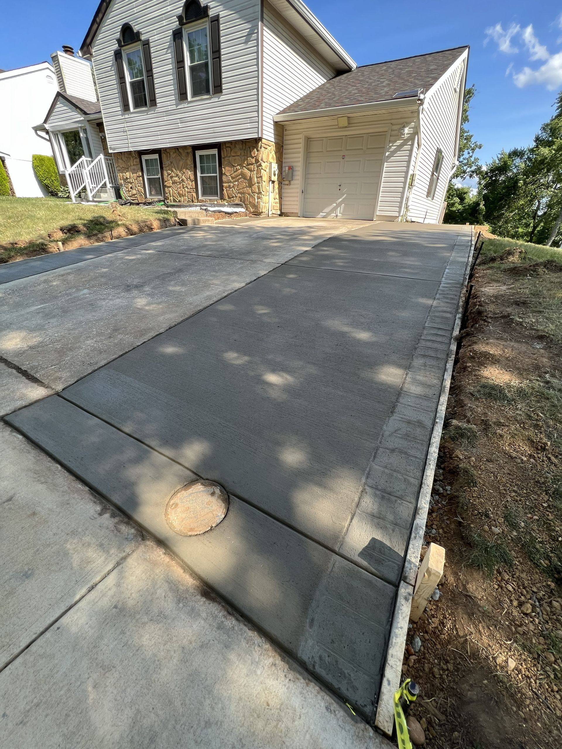 Concrete driveway leading to a two-story house with a garage and sloped walkway.