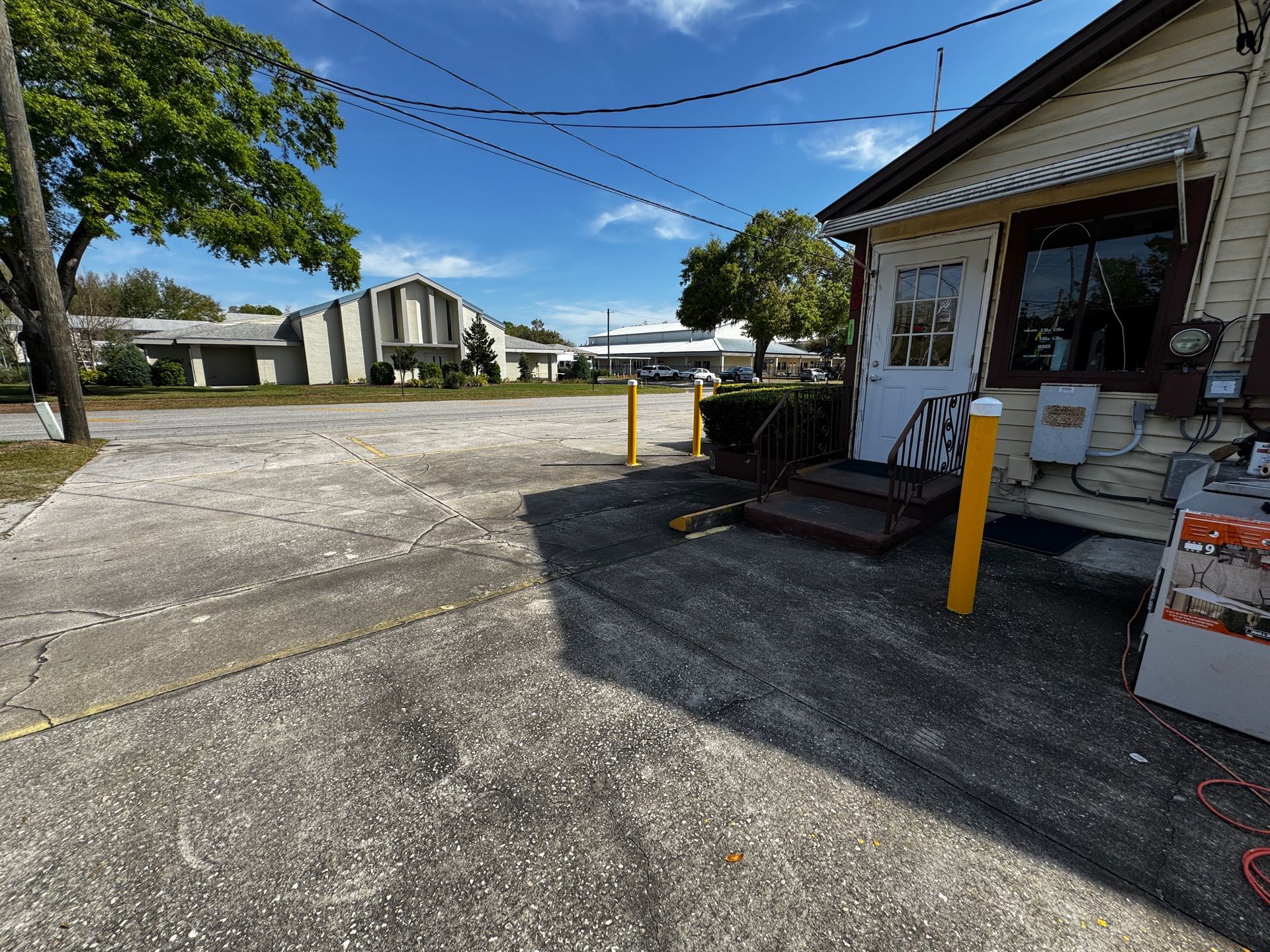 Sunny parking lot beside a small storefront with a ramp and yellow bollard