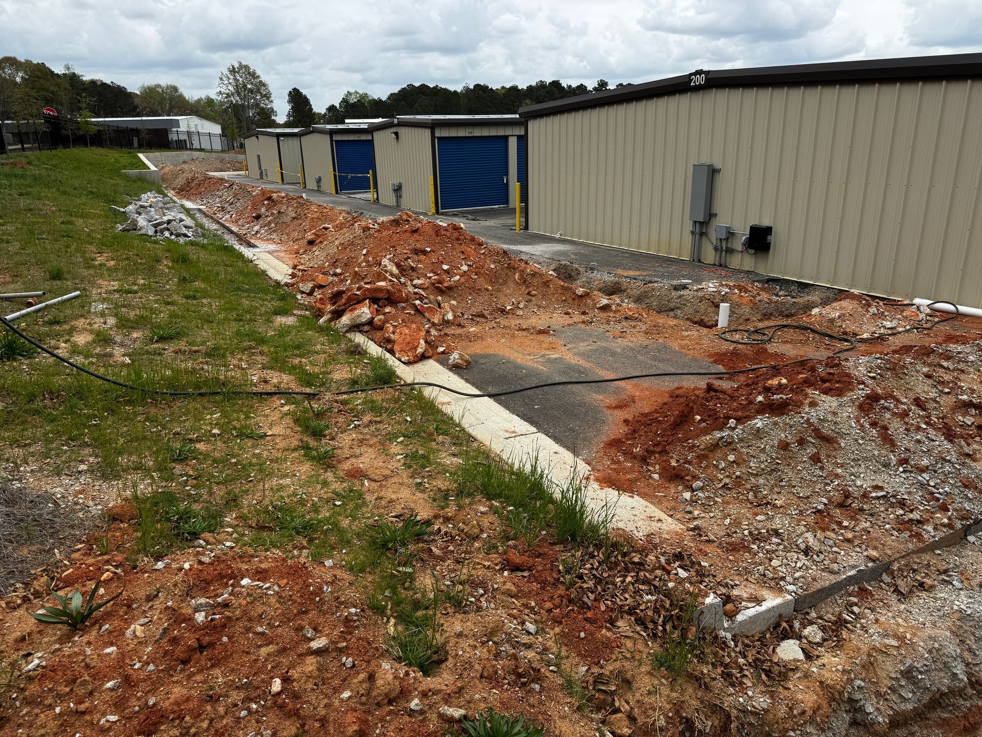 Collapsed brick pile beside a beige industrial building, with a blue door and a damaged concrete path.