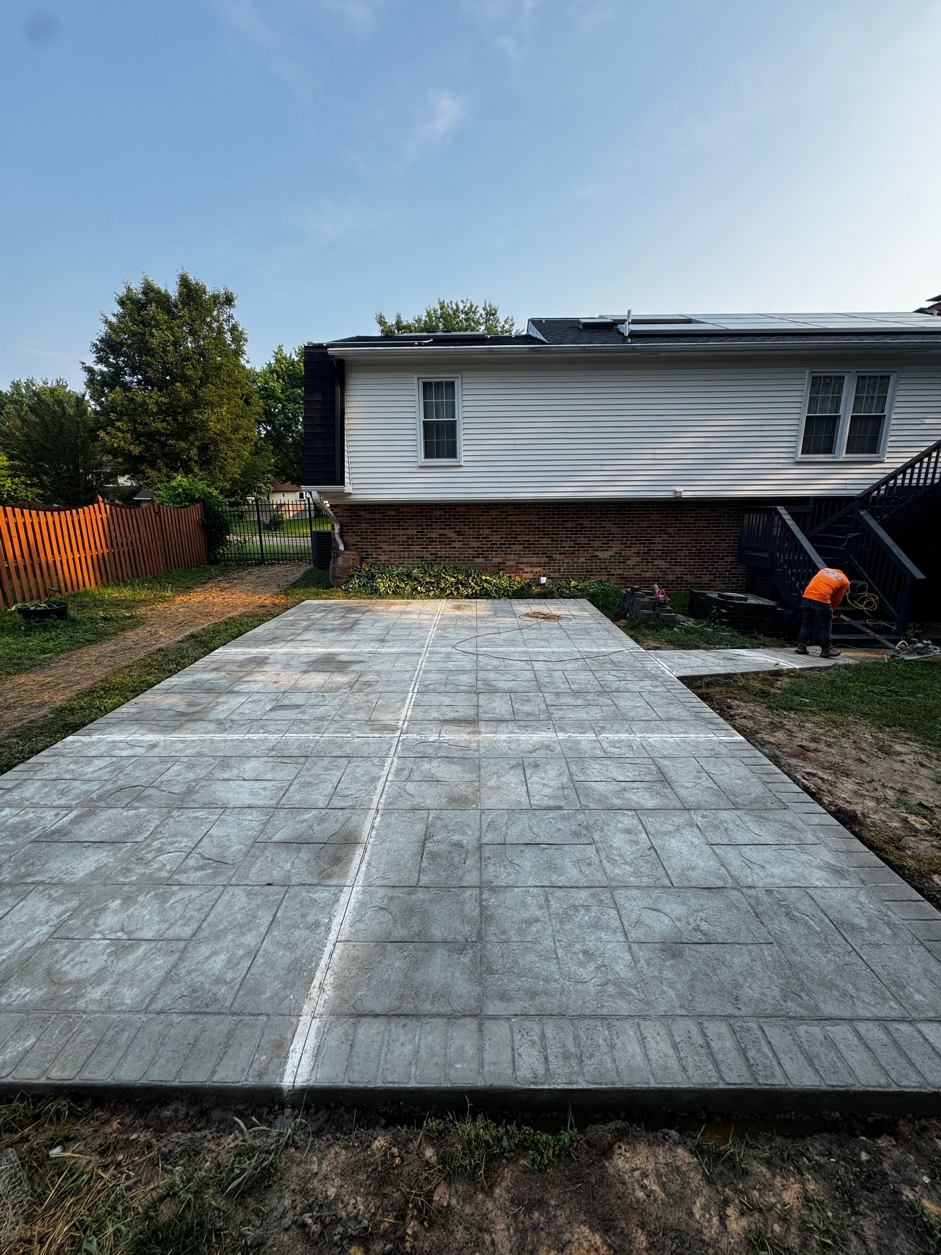 Concrete driveway leading to a white house with a brick foundation and a small yard.