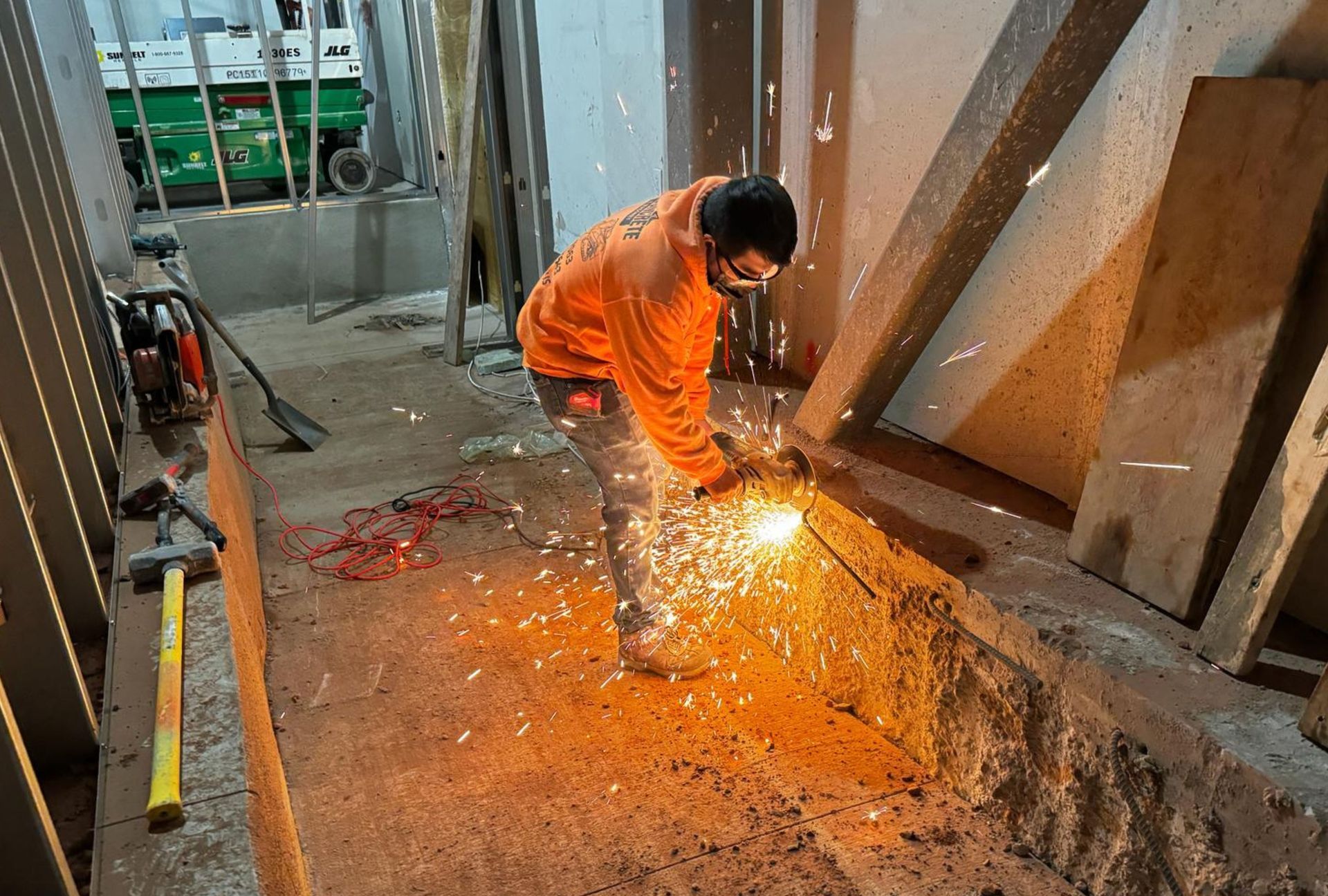 Worker in orange safety gear cutting metal with a grinder, sparks flying in an industrial workspace