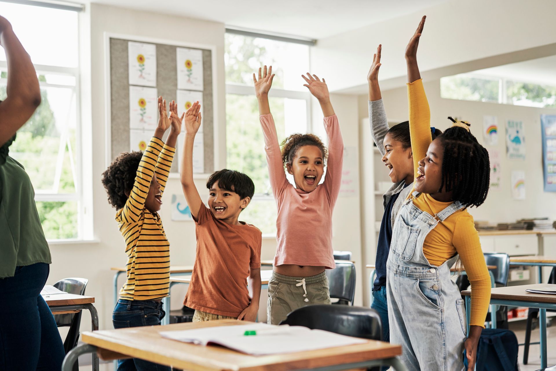 Children in a classroom with arms raised; joyful expressions.