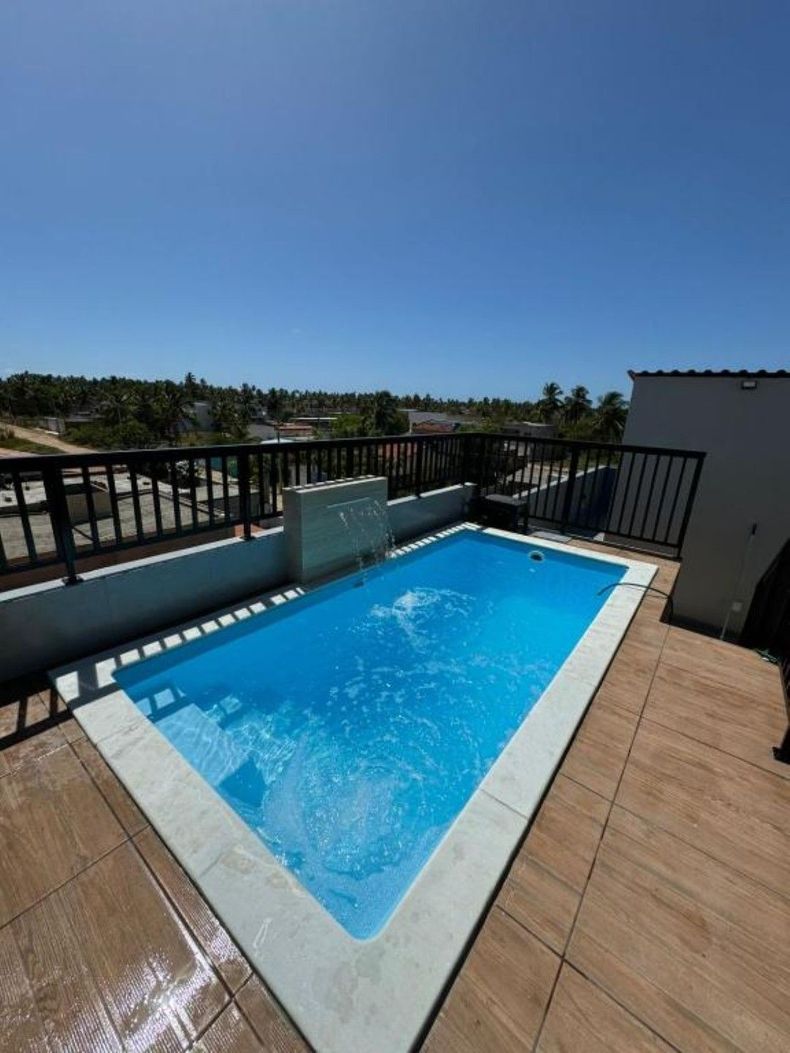 Pequena piscina na cobertura com água azul brilhante, corrimão preto e céu claro acima do deck externo.