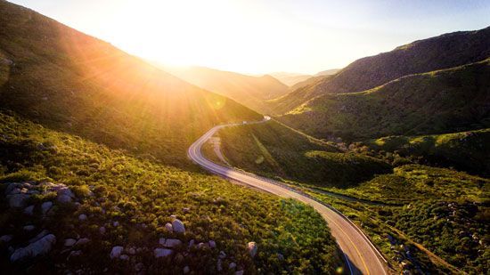 Winding road through lush green mountains bathed in warm sunlight.