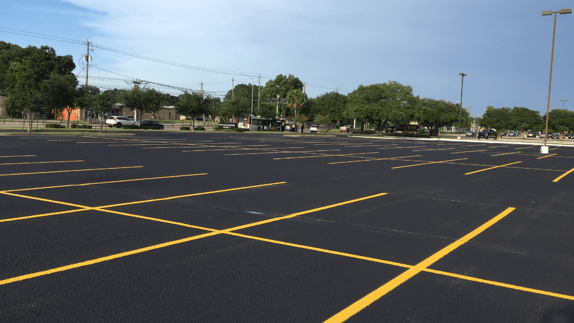 An empty parking lot with yellow lines and trees in the background