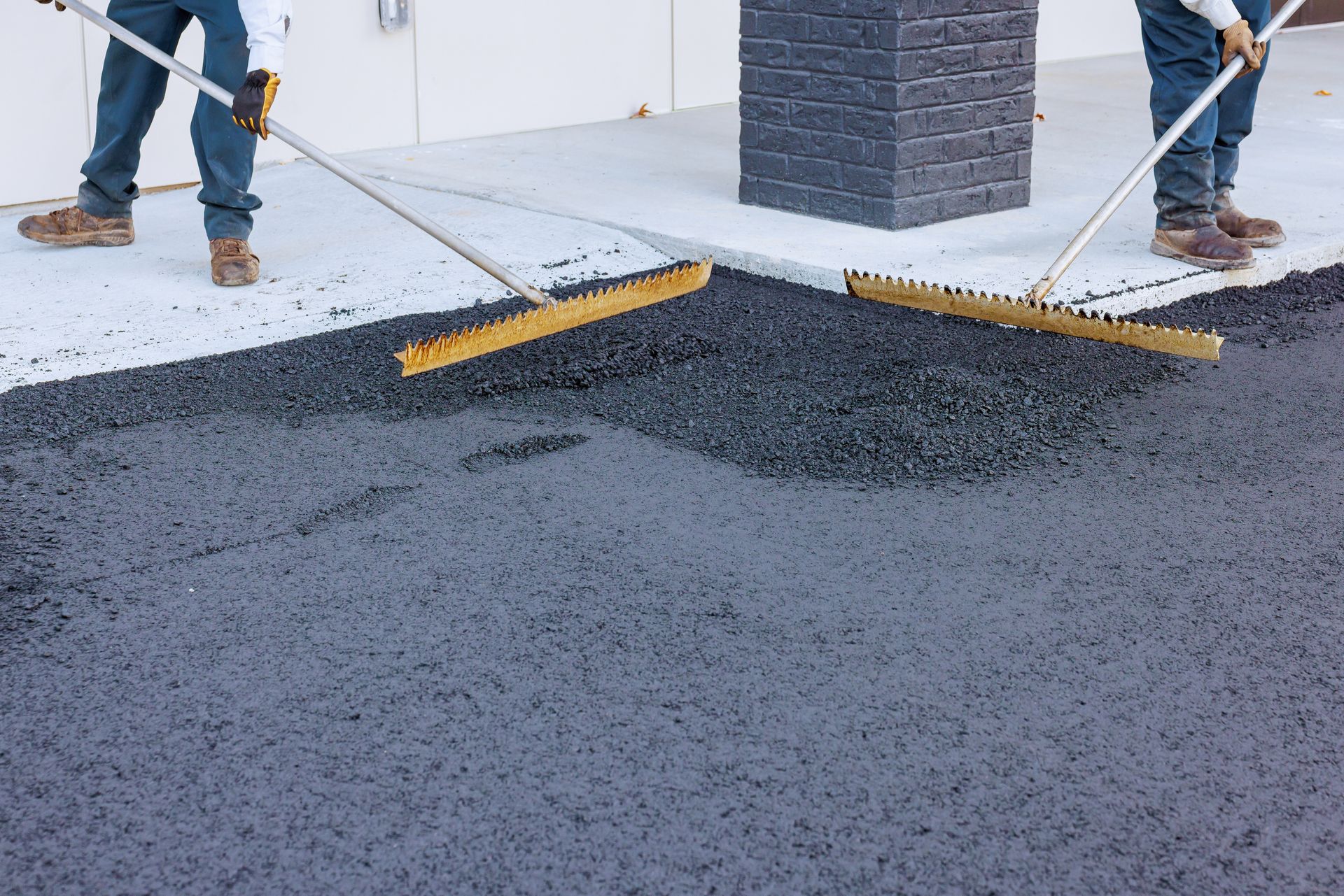 Workers spreading fresh asphalt during parking lot resurfacing.