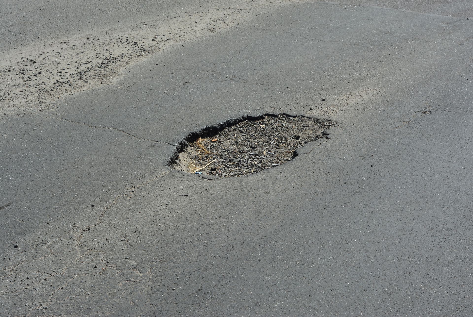 Pothole in asphalt road needing paving repair services to fix broken street pavement. 