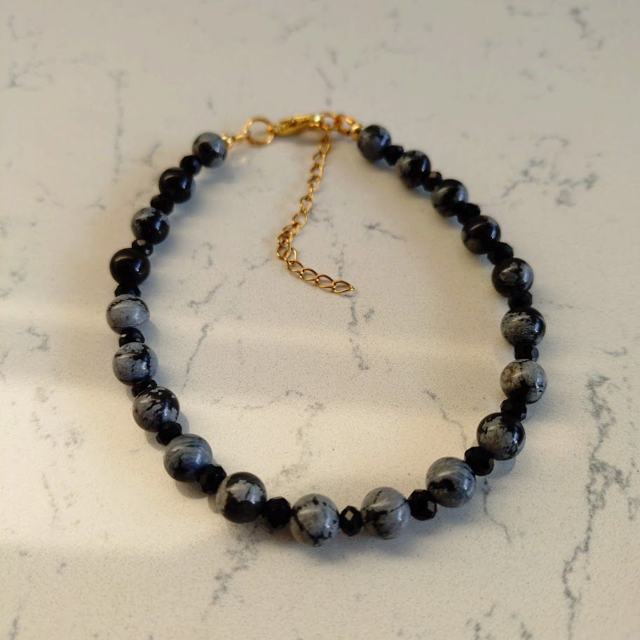 Chique armband van snowflake obsidiaan kralen van 6mm met zwarte facettussenkralen van 4mm en gouden stainless steel sluiting