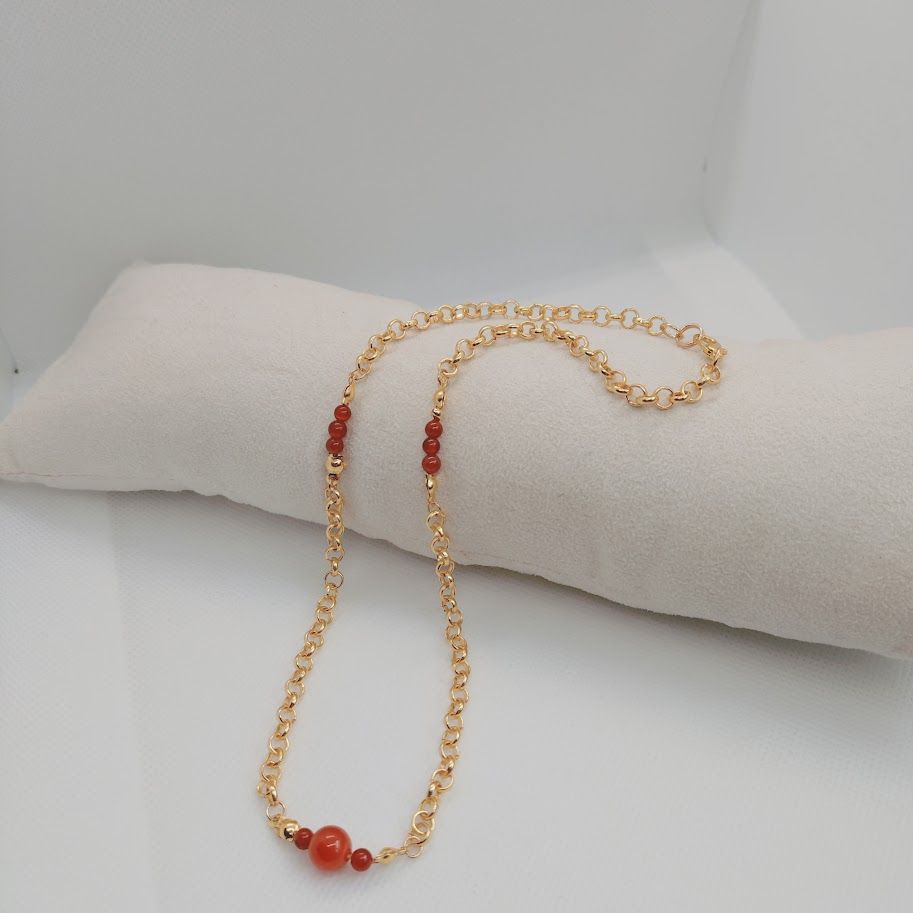 Stainless steel schakelketting met kleine carneool tussenkralen liggend op een kussentje