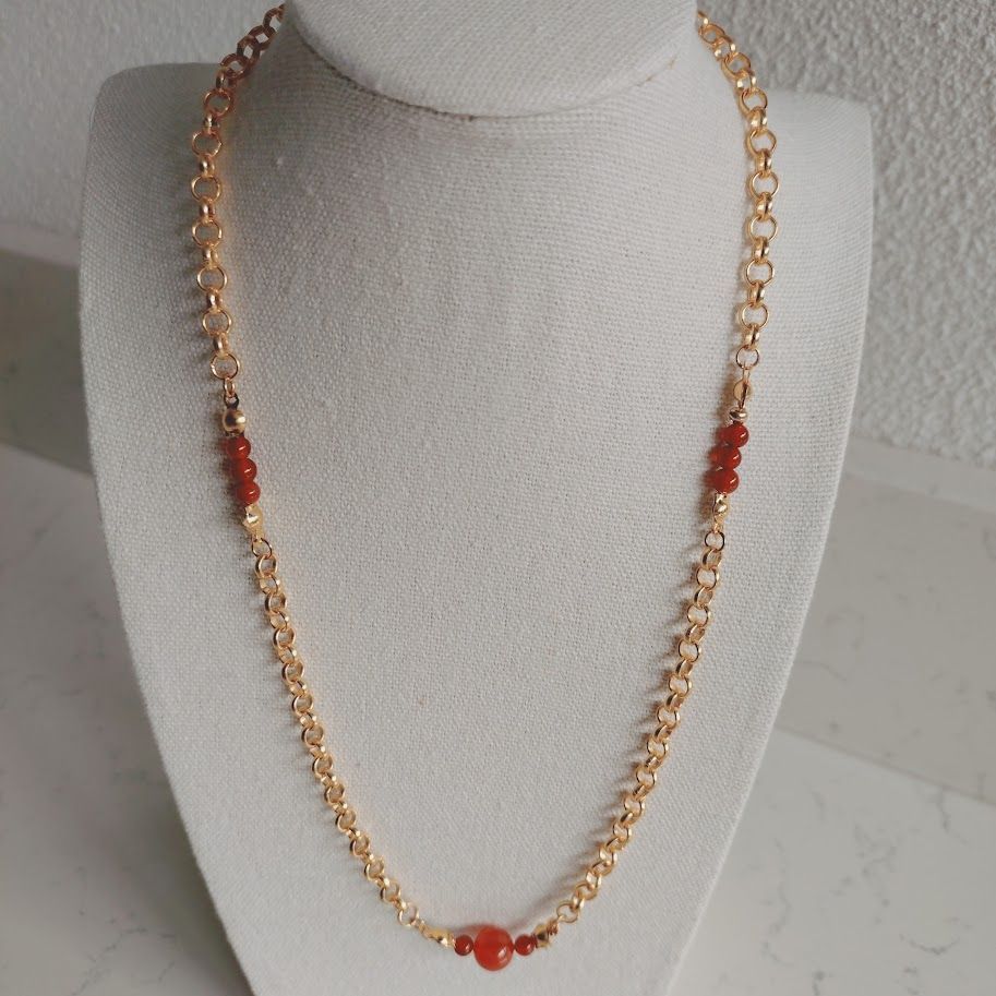 Stainless steel schakelketting met kleine carneool tussenkralen liggend op een kussentje