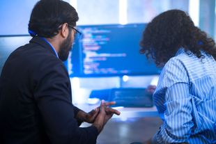 Two people looking at a computer screen, likely reviewing code, in a modern office.