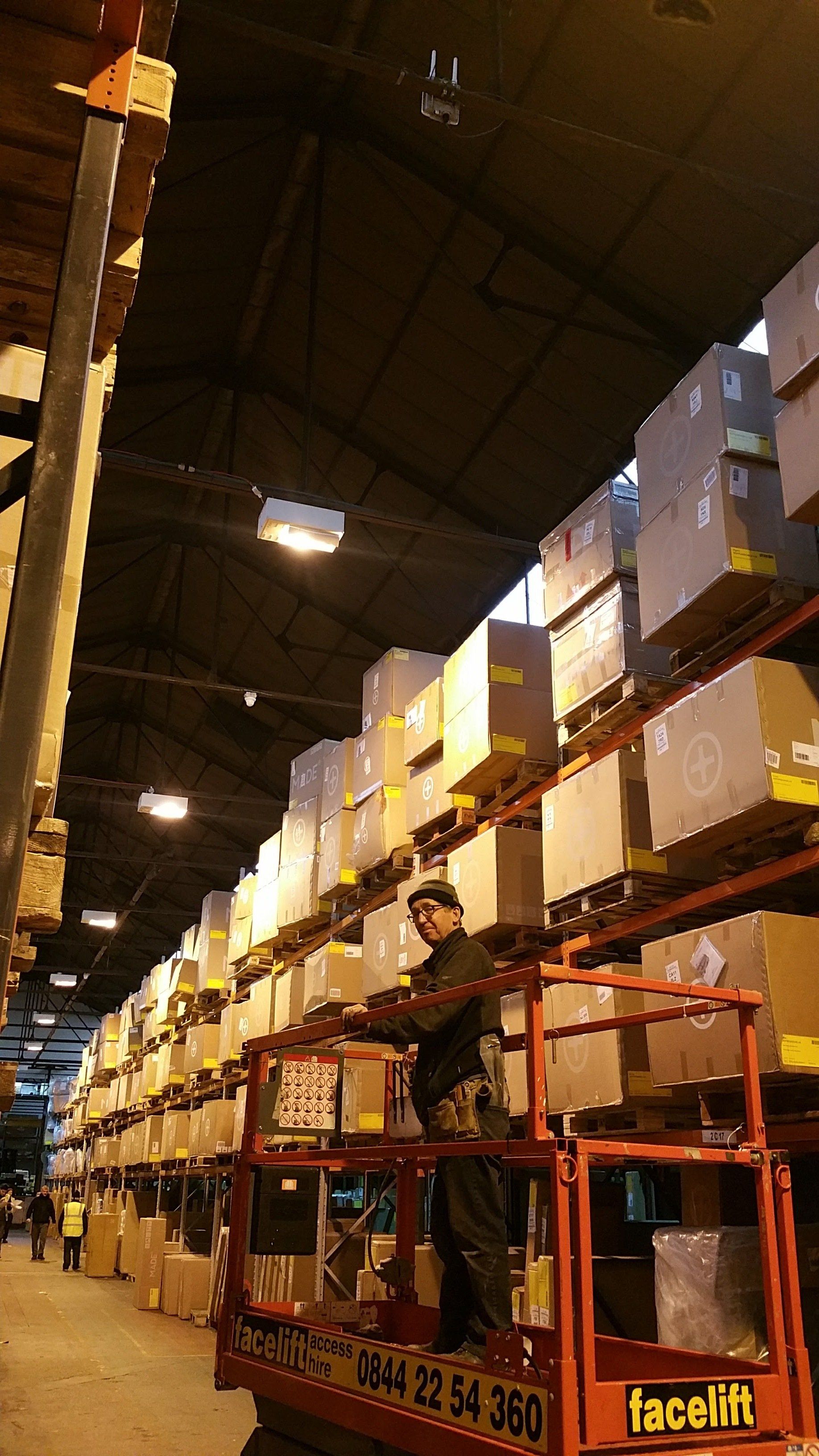Warehouse aisle with stacked cardboard boxes on shelves and a red forklift below.