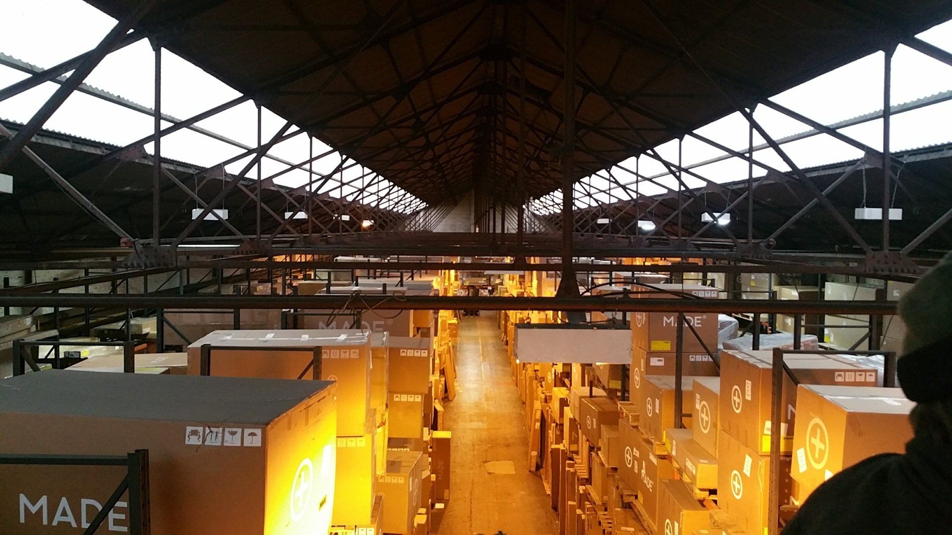 Indoor industrial hall with rows of lit stalls and warm orange lights under a high metal roof