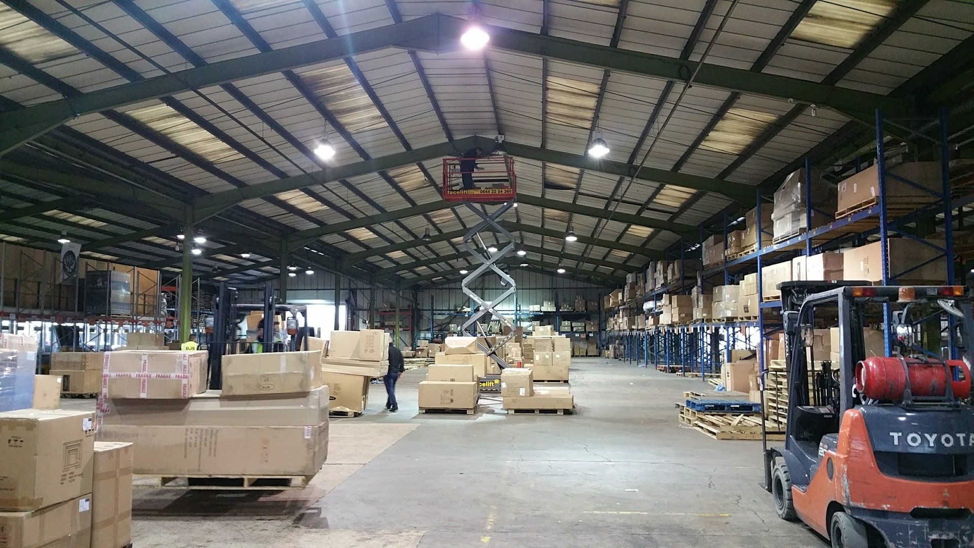 Warehouse interior with stacked cardboard boxes and an orange forklift under a high metal roof