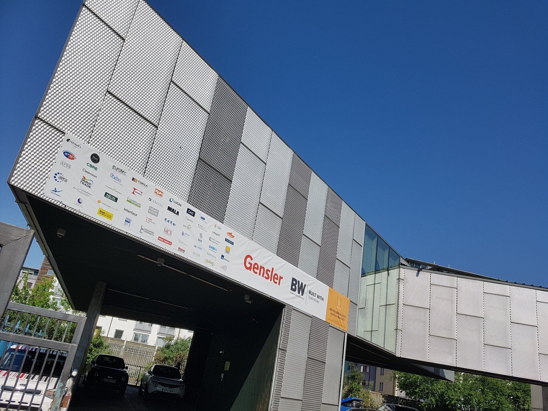 Modern silver building entrance with sponsor banners under a clear blue sky