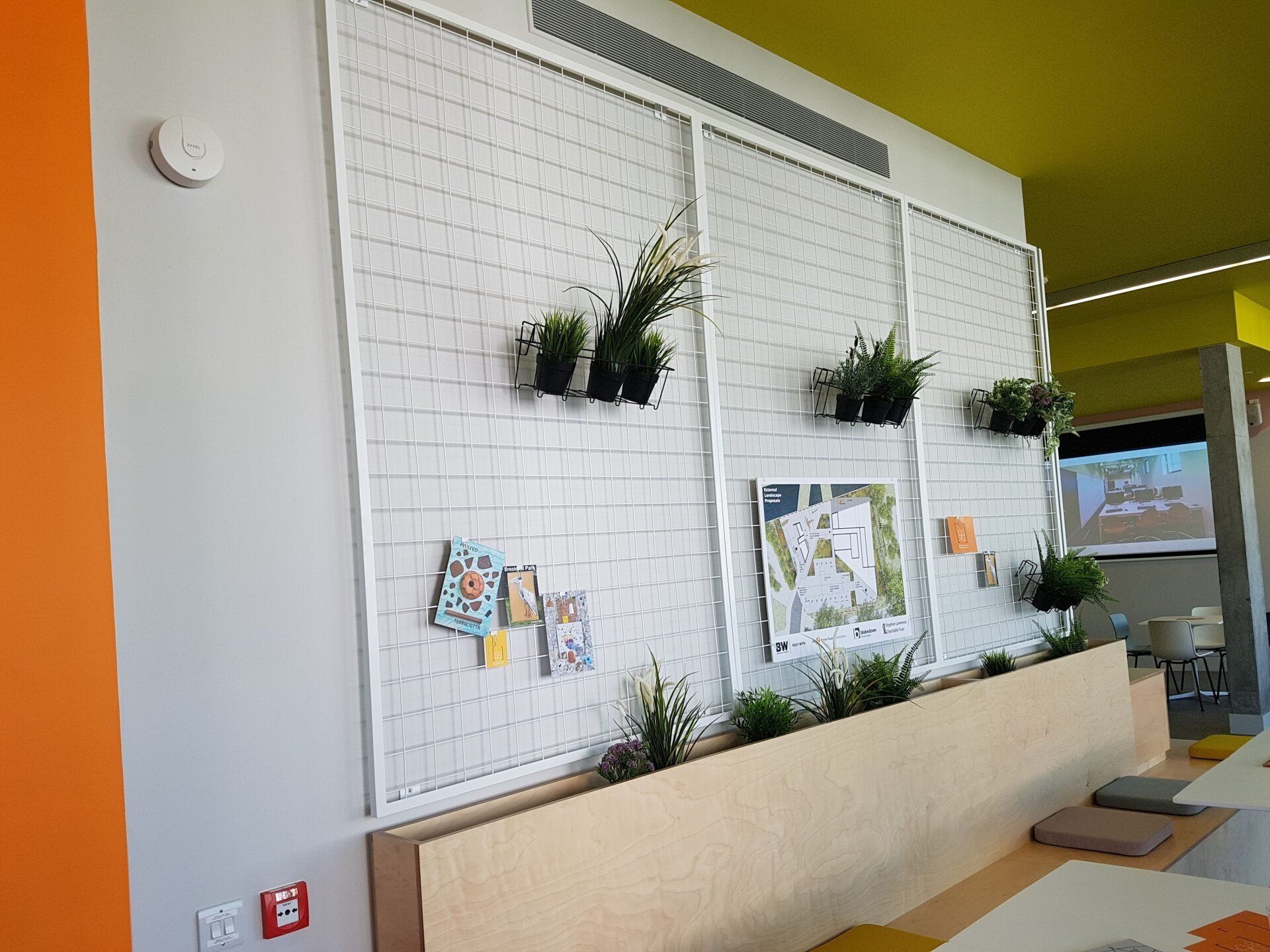 Indoor wall with hanging potted plants, white brick panel, and a bench in a bright modern hallway.