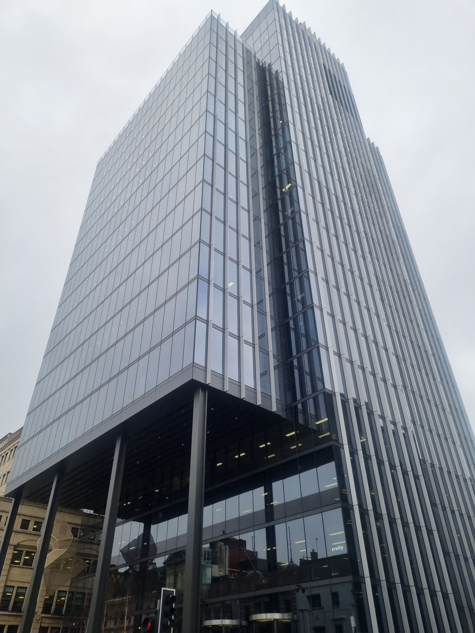 Modern glass office tower with a reflective facade against a cloudy sky