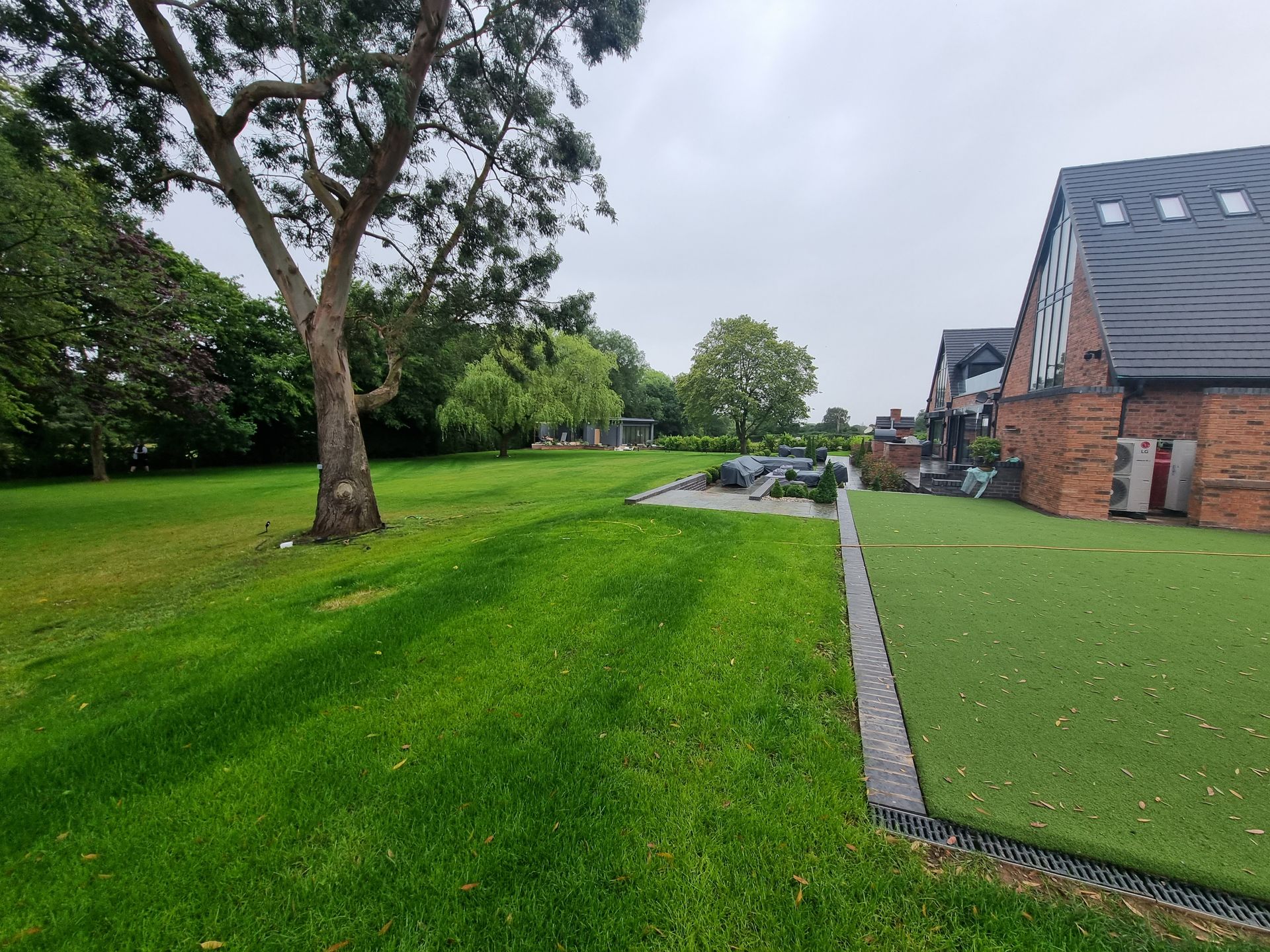 Grassy park beside brick houses and a paved path under cloudy skies