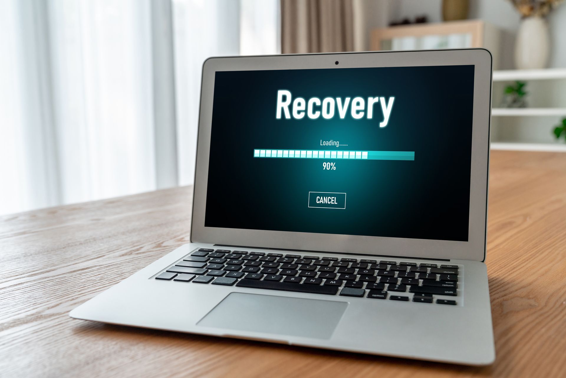 Laptop on a wooden table displaying a “Recovery” screen with a progress bar.