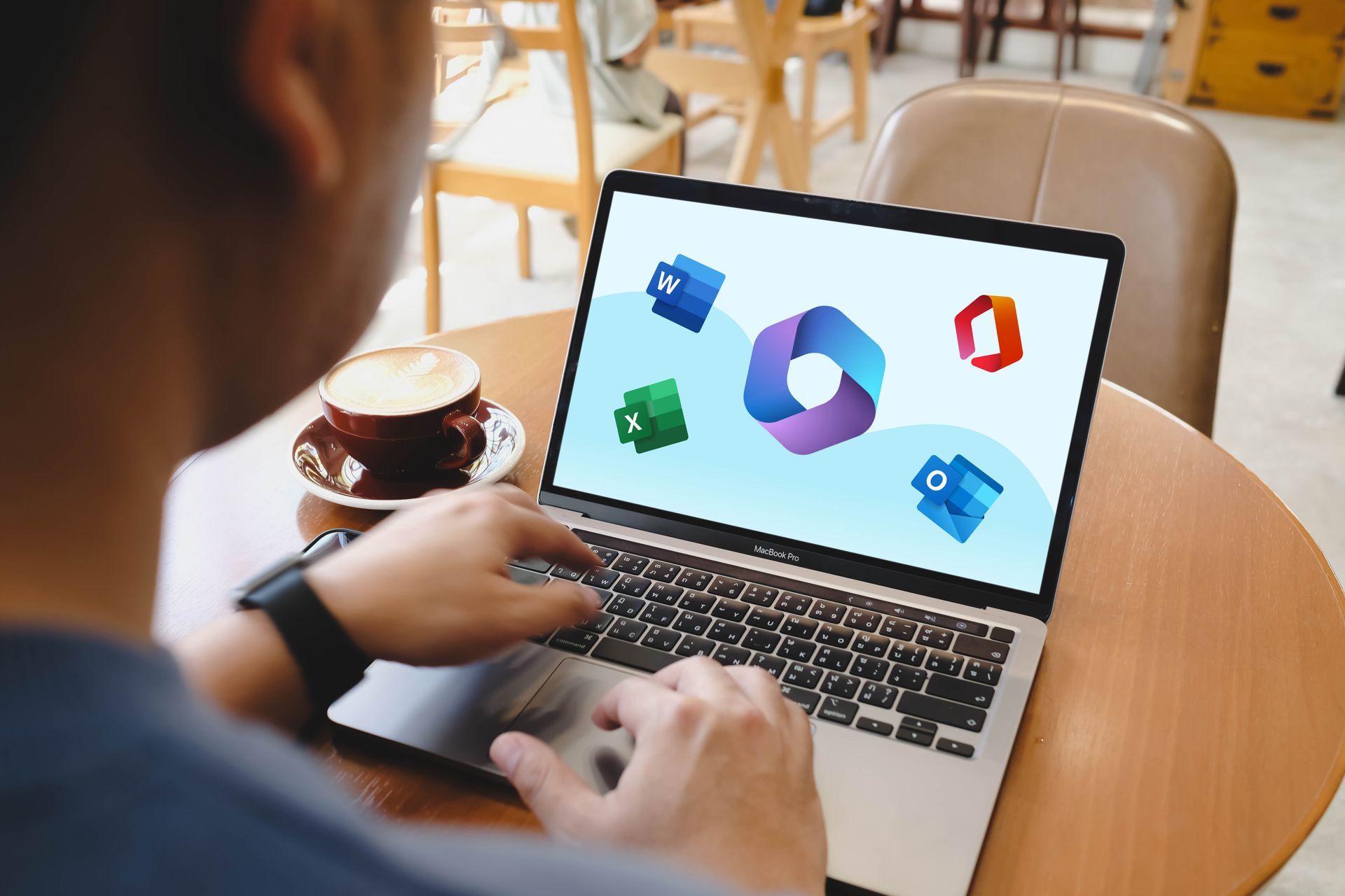 Person using a laptop with Microsoft 365 icons on screen at a café table