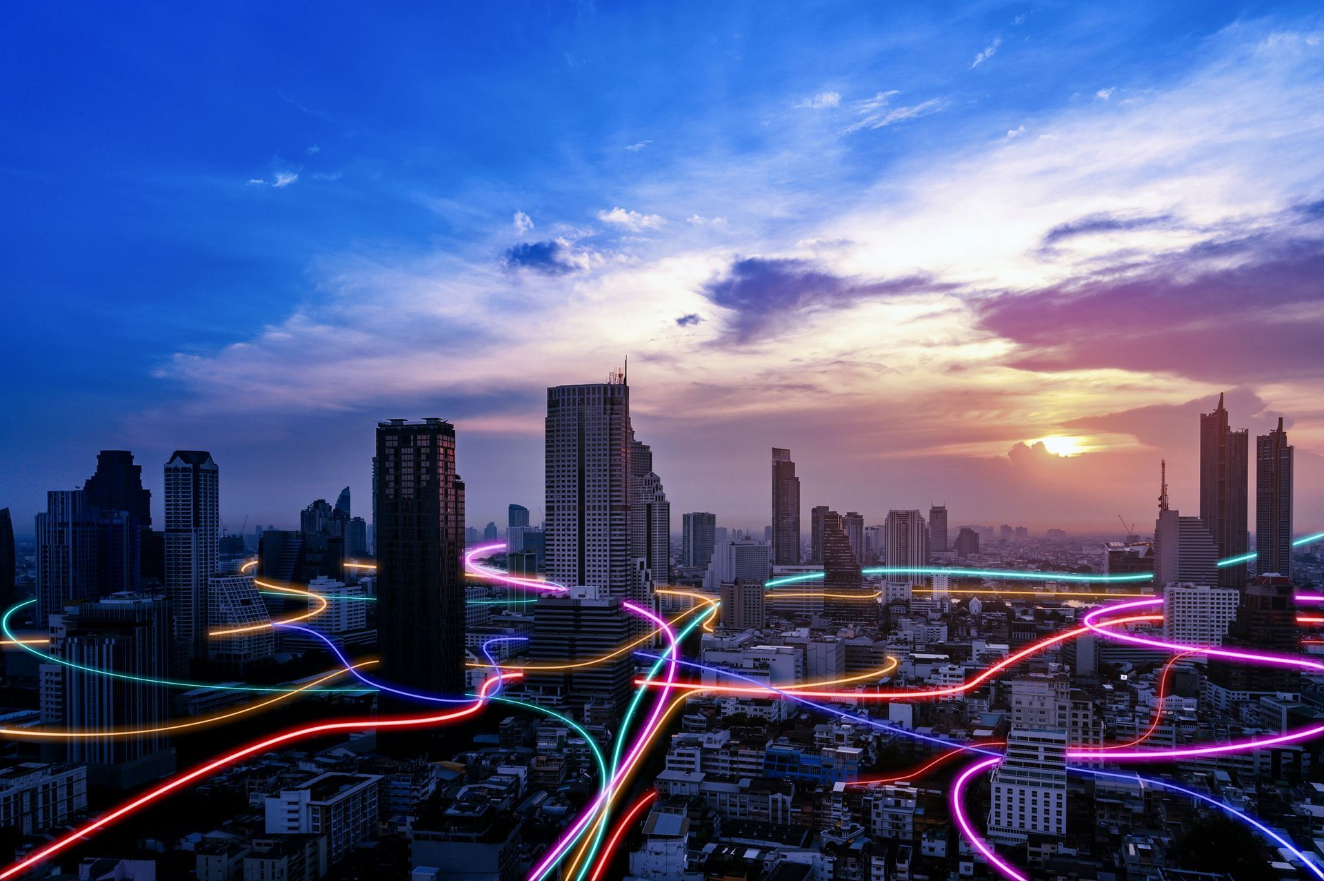 City skyline at sunset with glowing pink and blue light trails weaving through roads.