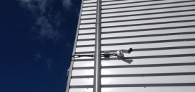 White metal siding with a mounted security camera against a blue sky