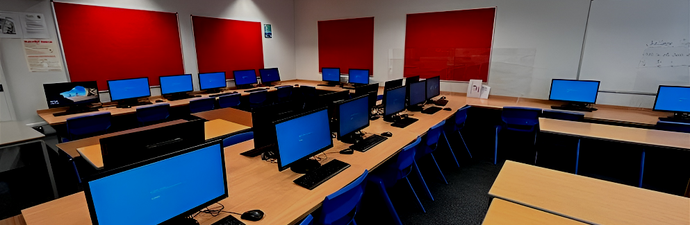 Classroom with rows of desks and laptops, blue screens glowing against red and white walls.