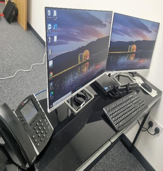 Office desk with dual monitors, keyboard, desk phone, and cables in a corner workspace