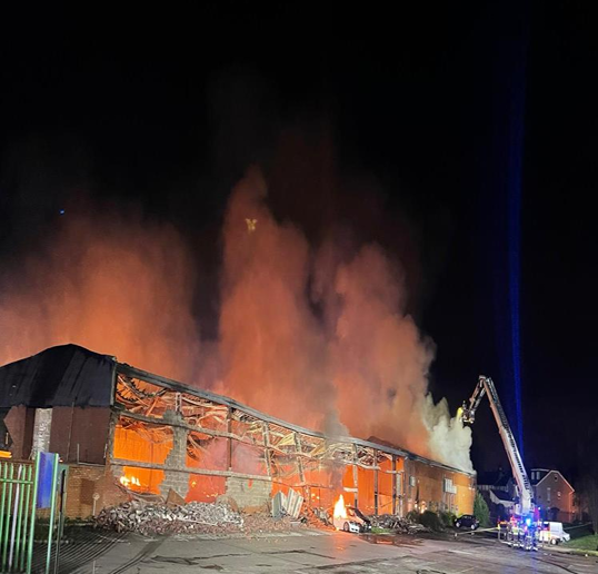 Firefighters battle a large blaze engulfing a building at night, with heavy smoke and flames rising.