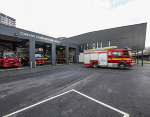 Fire station with red fire engines parked at the bay, one engine driving out onto the forecourt