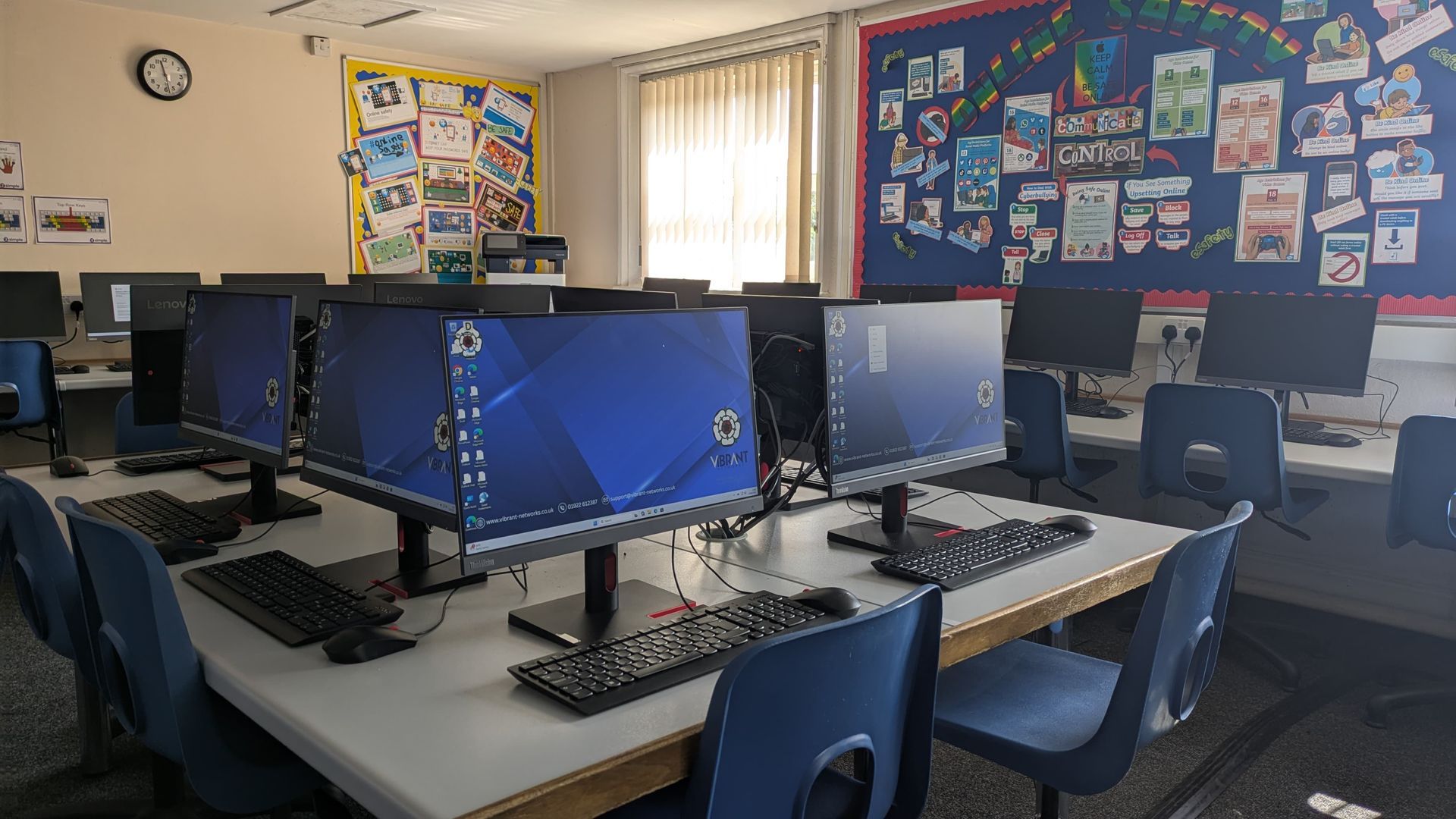 School computer lab with several desktop monitors on tables and classroom posters on the walls.