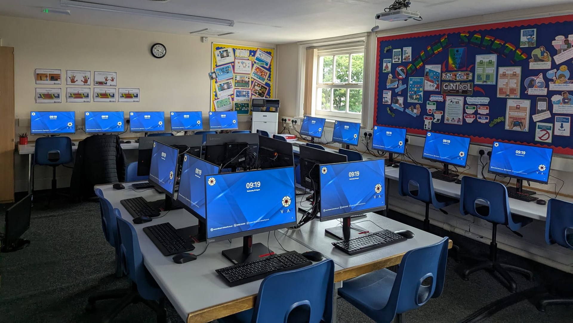 School computer lab with rows of desktop monitors on tables in a classroom