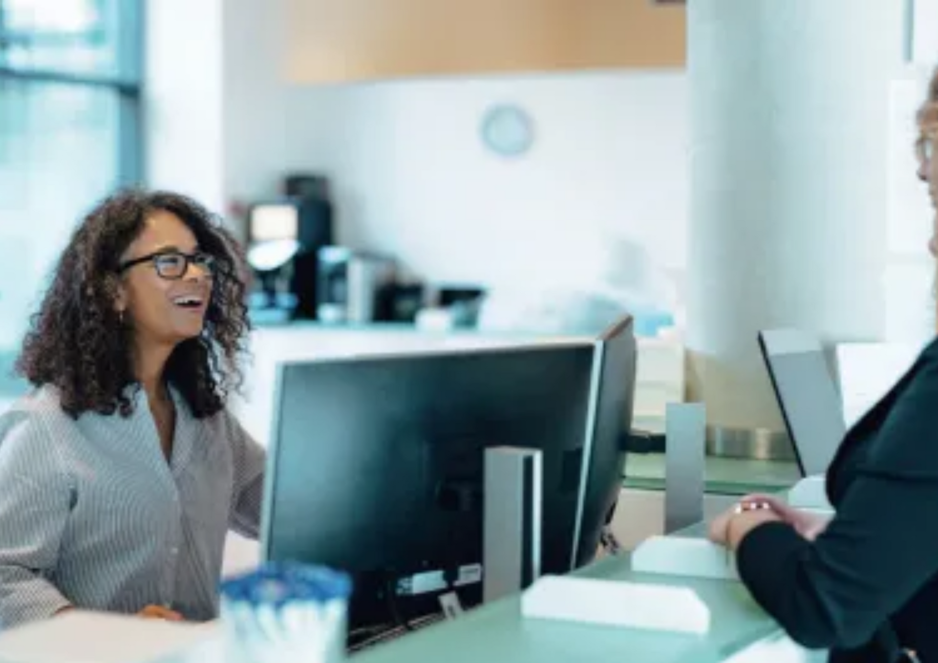 Two people talking at a reception desk in a bright office lobby