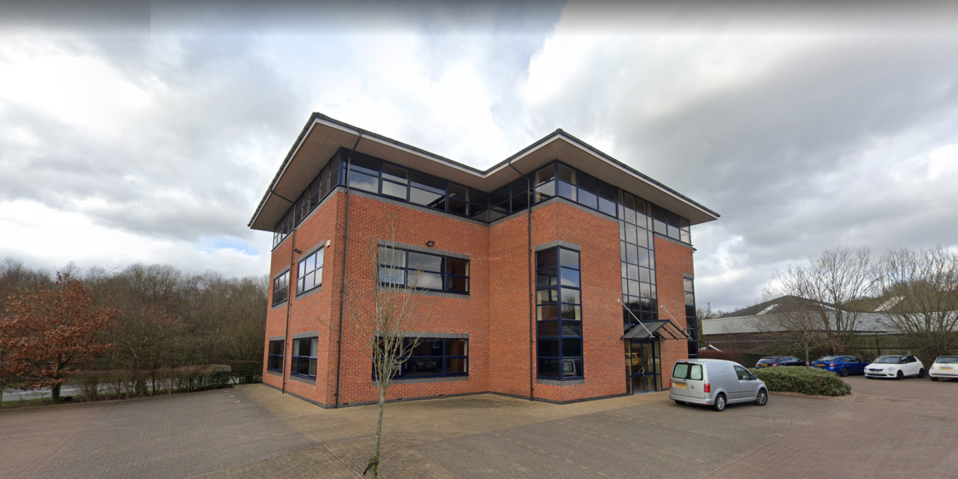 Red brick office building with large windows and a parked car on a cloudy day
