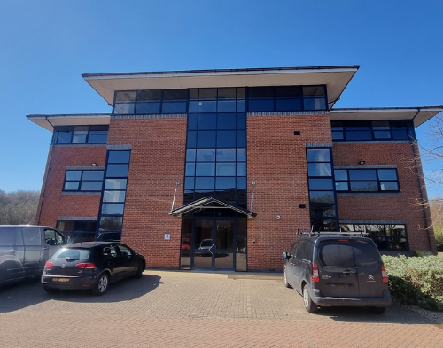 Modern brick office building with large glass windows and parked cars in front under a clear blue sky