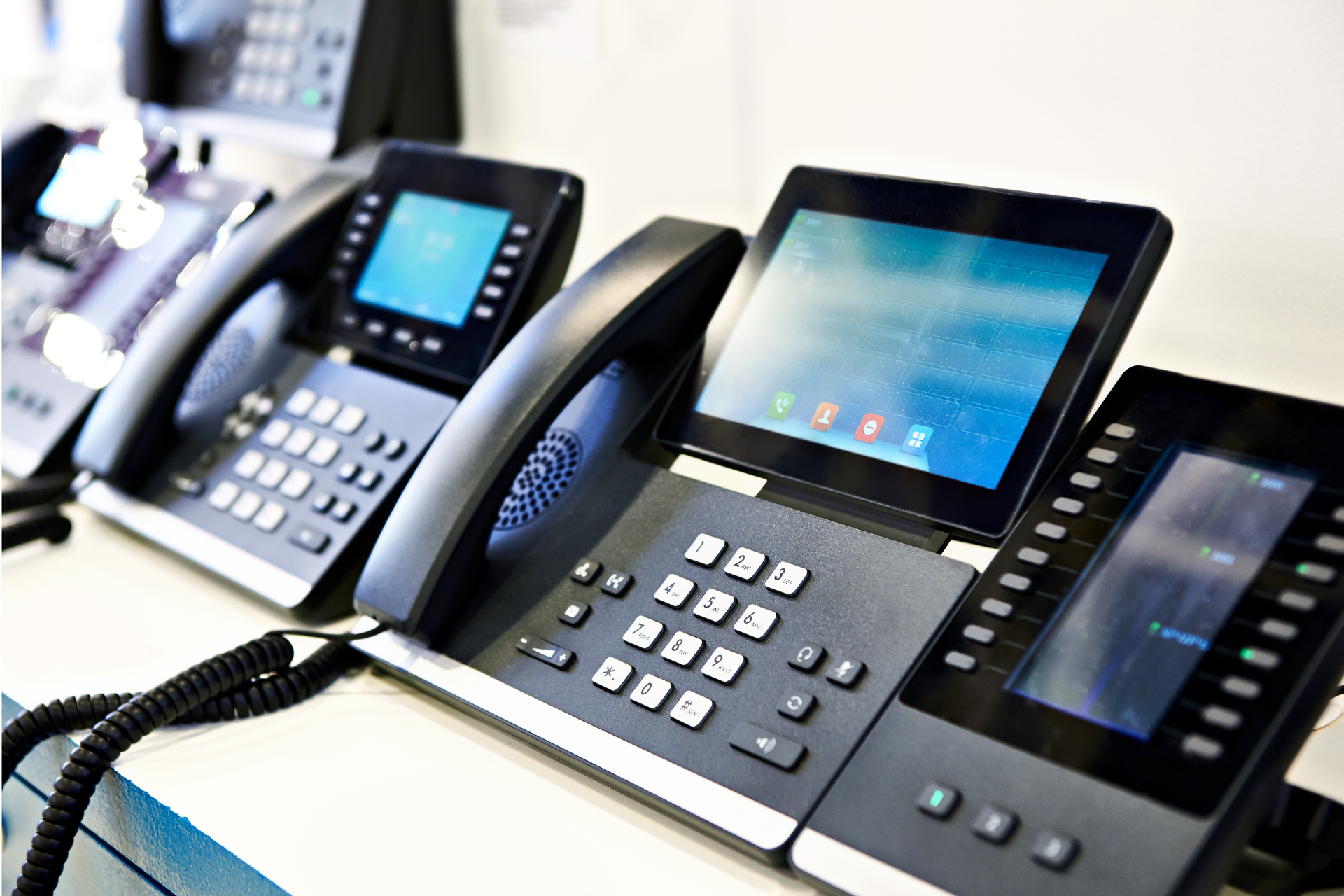 Row of black office VoIP phones with digital displays on a conference table