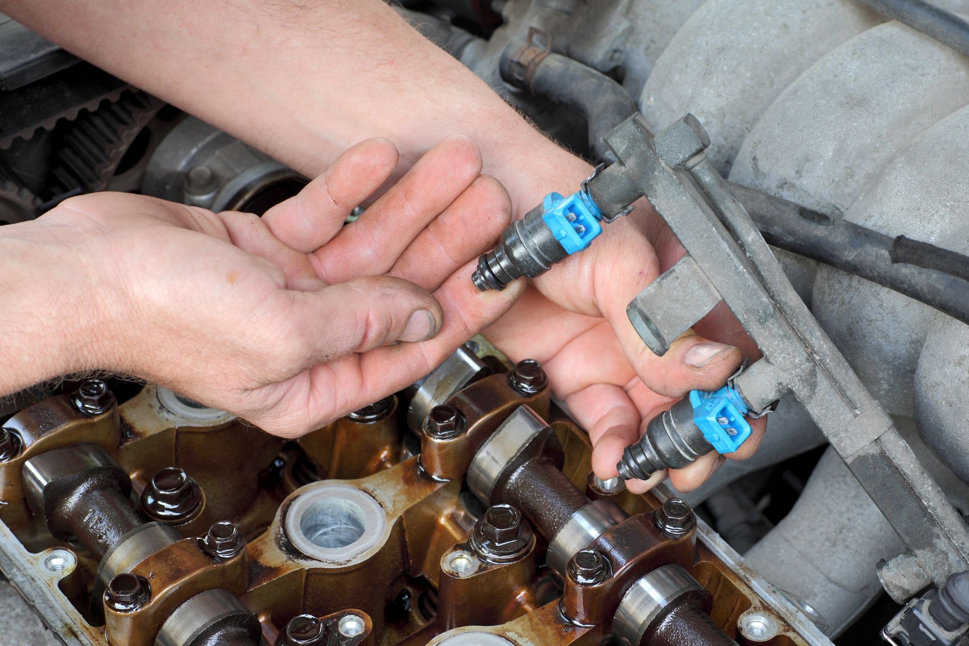 Hands installing fuel injectors on an engine with exposed camshafts.
