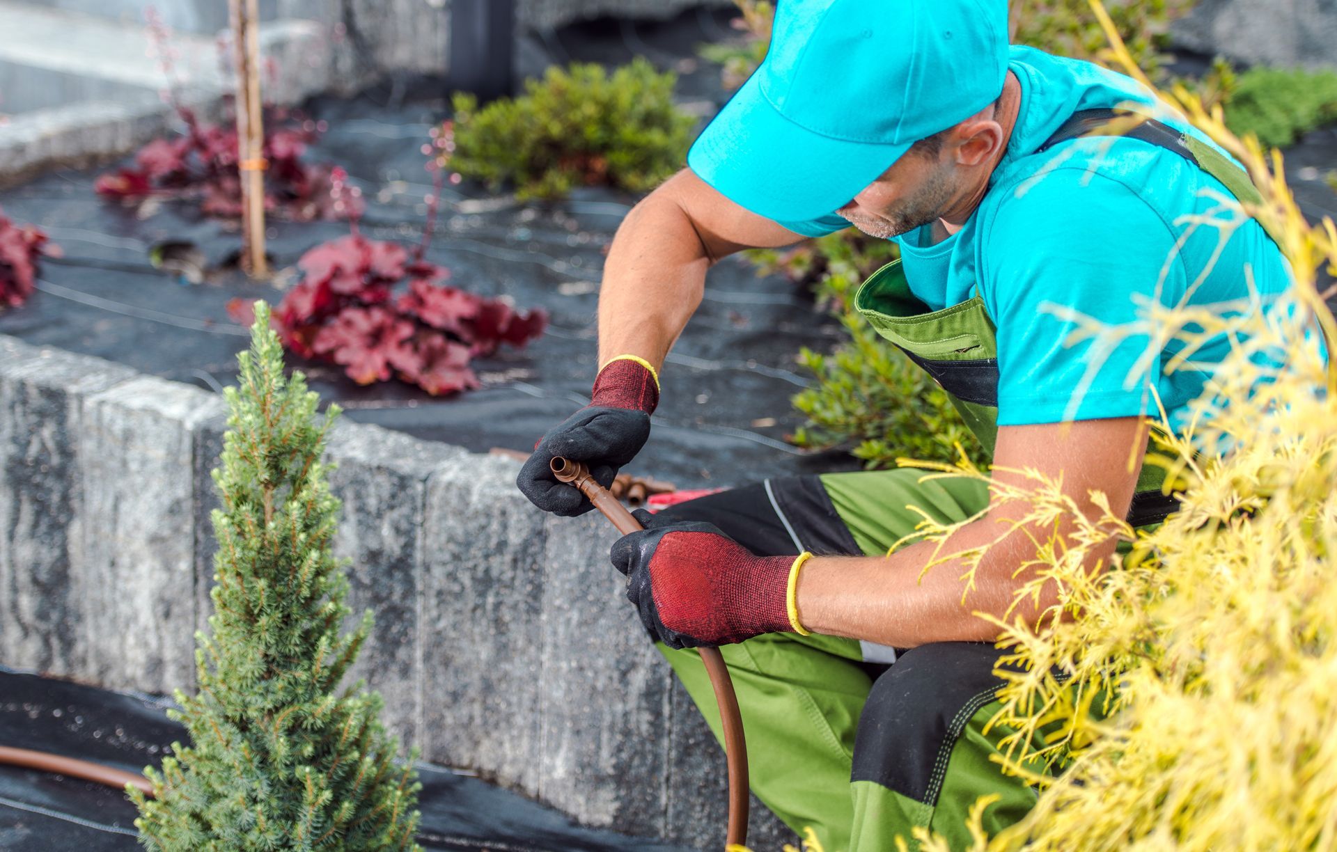 Gardener repairing irrigation system in a landscaped garden during a sunny afternoon.