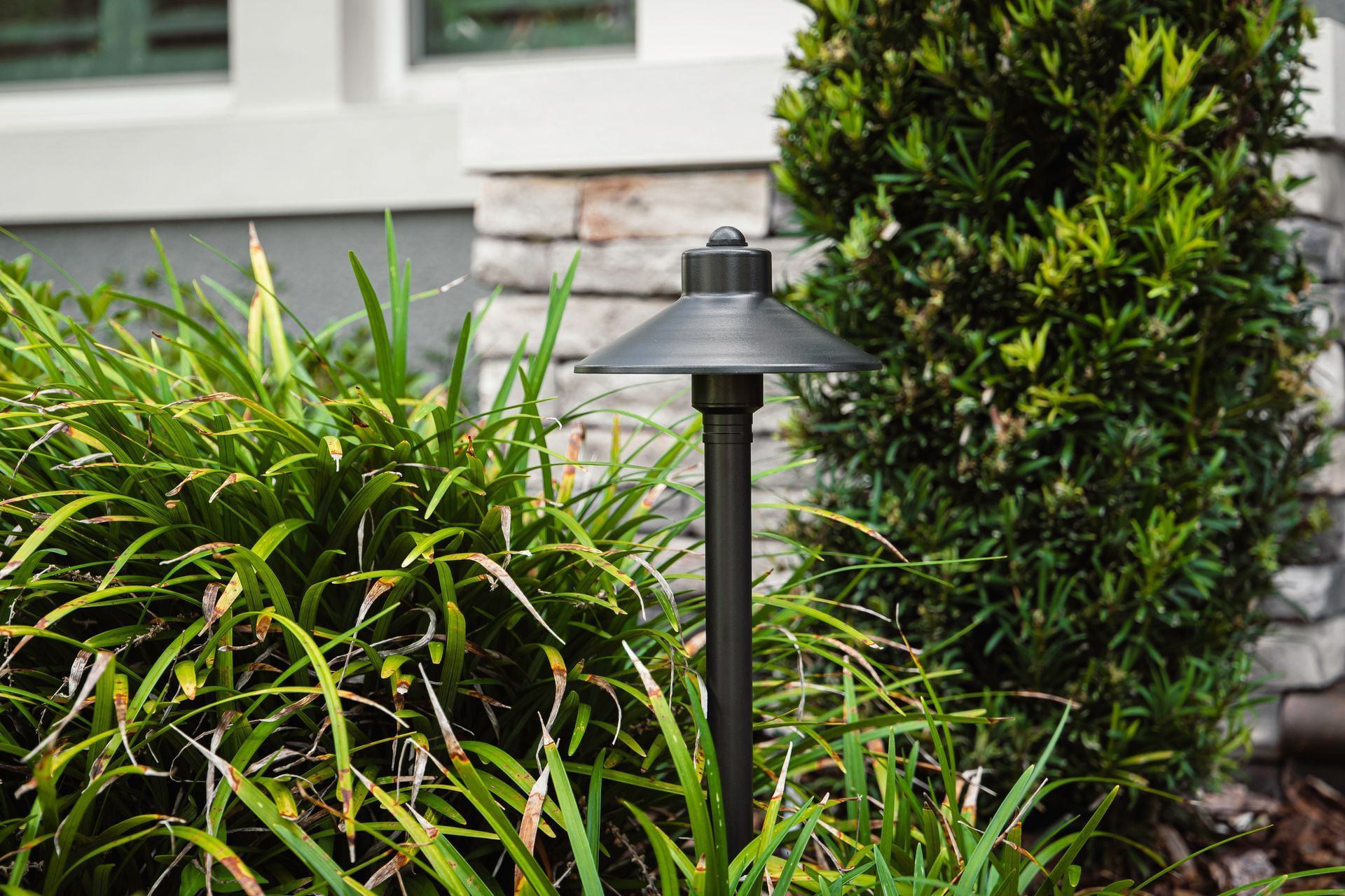 Black landscape light among green shrubs beside a house exterior