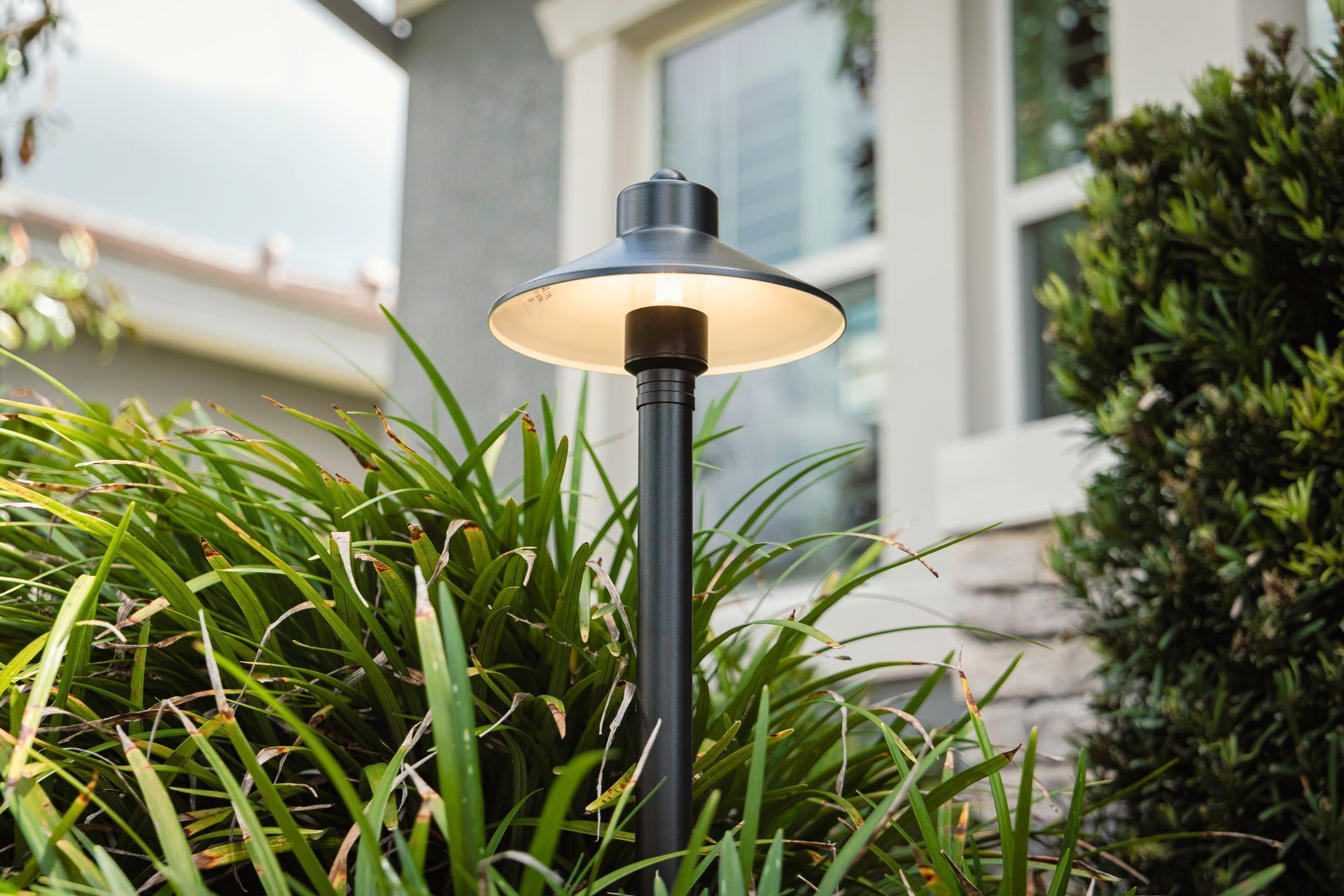Black garden lamp among green plants in front of a house