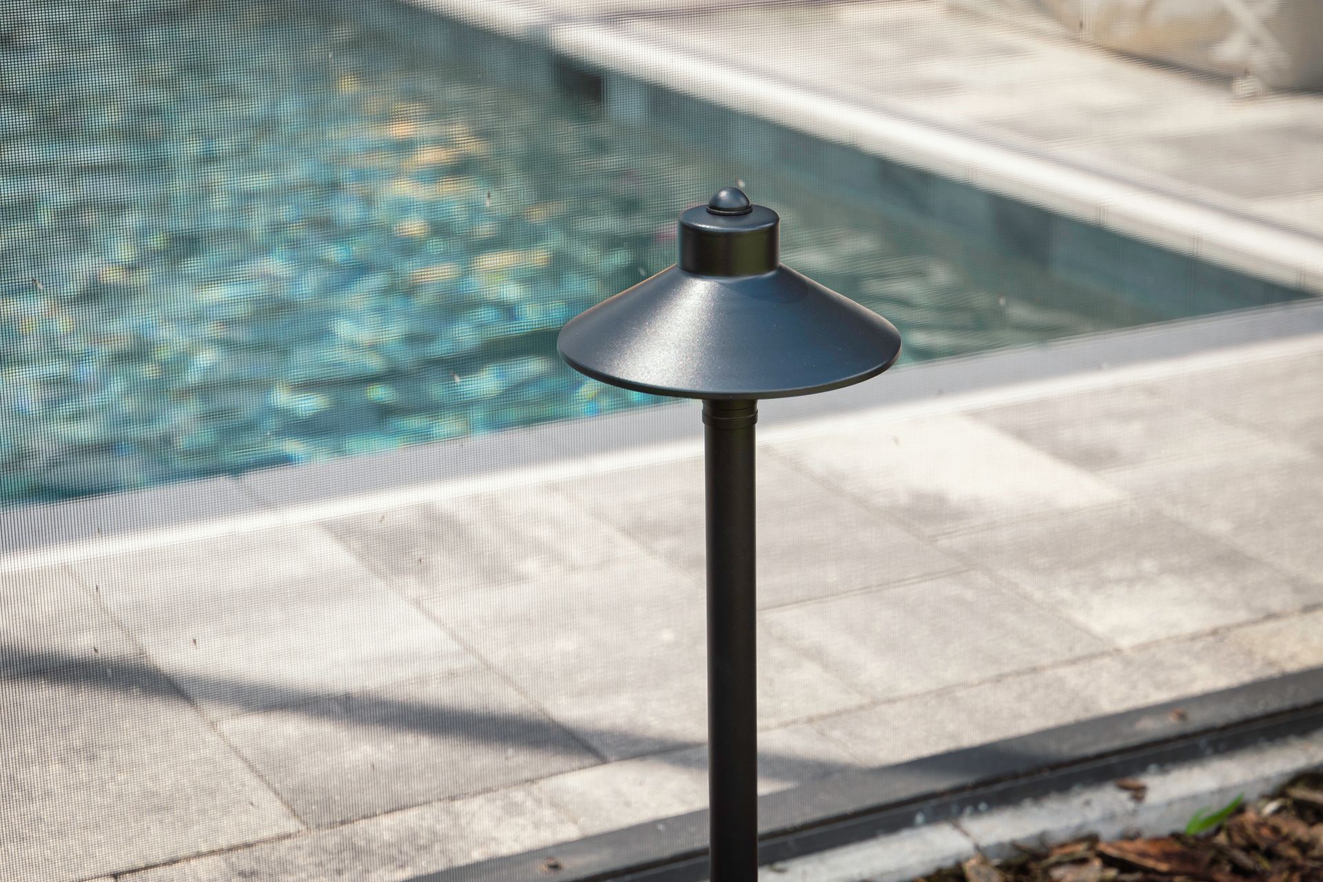 Black garden light beside a pool with blue water and stone coping