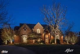 Lit brick house exterior at dusk with warm porch and landscape lights under a blue evening sky