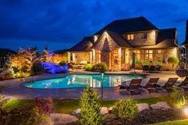 Luxury stone house at dusk with lit pool, lounge chairs, and landscaped garden